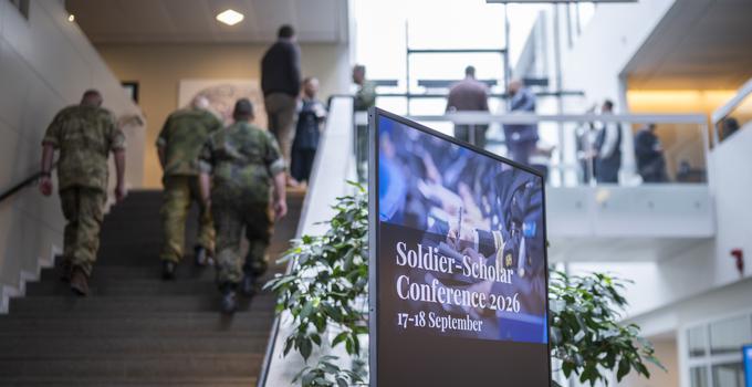 Militärer som går uppför en trappa samt skylt till konferens i FHS entré. 