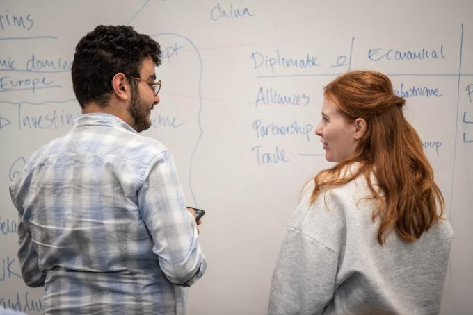Khalil Talhaoui och Emelie Moregård pratar med varandra och står vända mot en whiteboard-tavla med anteckningar.