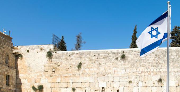 Israelisk flagga framför en stenmur. 