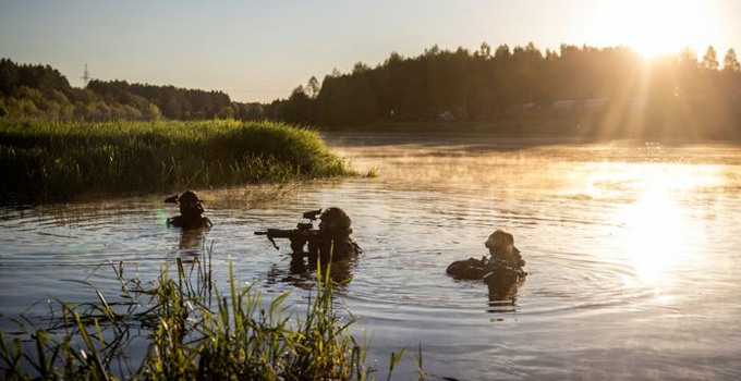 three soldiers walking in a lake with raised weaponsa