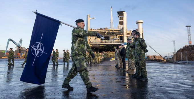 Militär som bär en Natoflagga framför en båt.