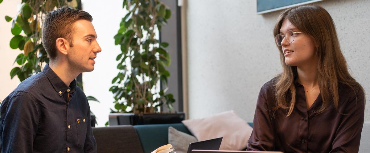 Två studenter i soffgrupp framför laptops.