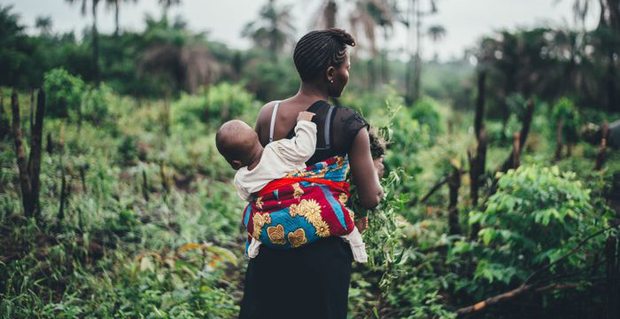 African woman with child on her back in a farm environment.