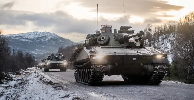 Stridsfordon på landsväg genom snöklätt landskap.