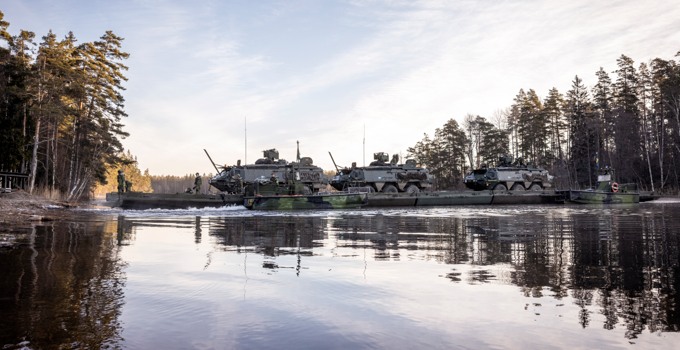 Stridsvagnar som passerar ett vattendrag i en skog. 