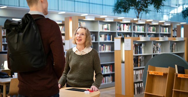 En kvinna som pratar med en man på ett bibliotek.