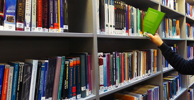En kvinna läser en bok på ett bibliotek.