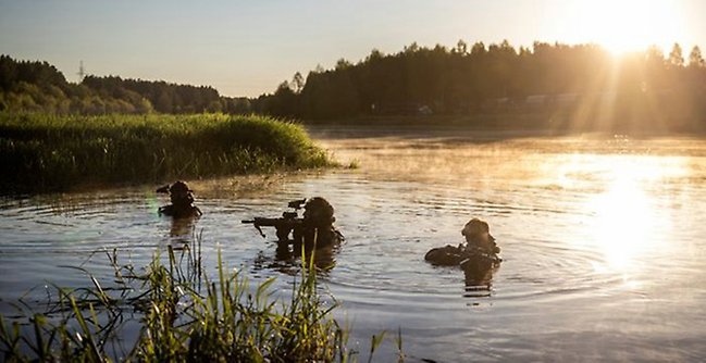 tre soldater går i en sjö med vapen höjda