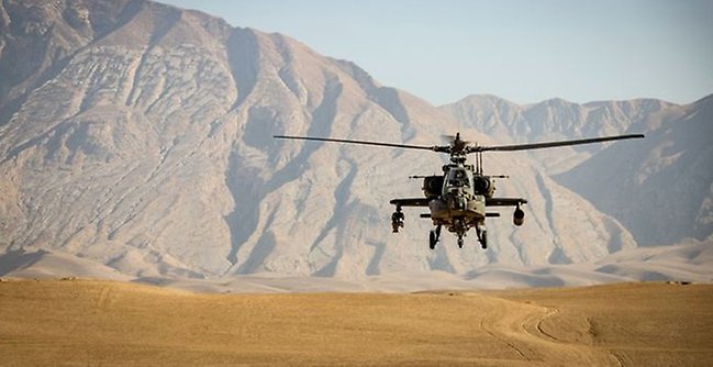 En militärhelikopter i luften framför berg i bakgrunden.