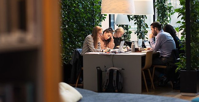 Studenter vid bord i biblioteket.