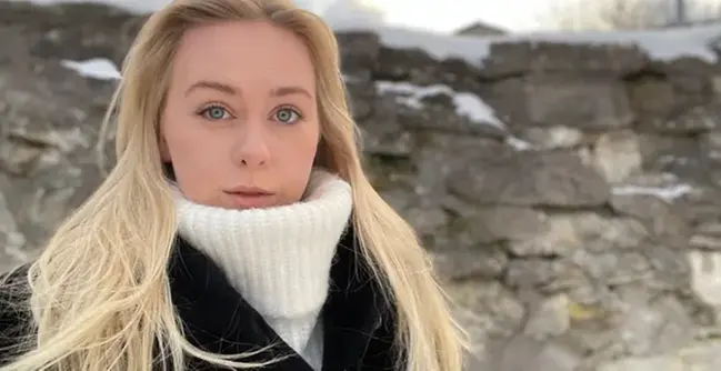 En kvinna med långt blont hår som bär en svart kappa.