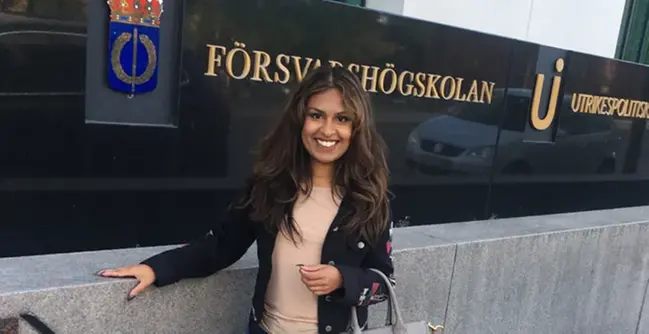 En kvinna som står framför en vägg med en handväska.